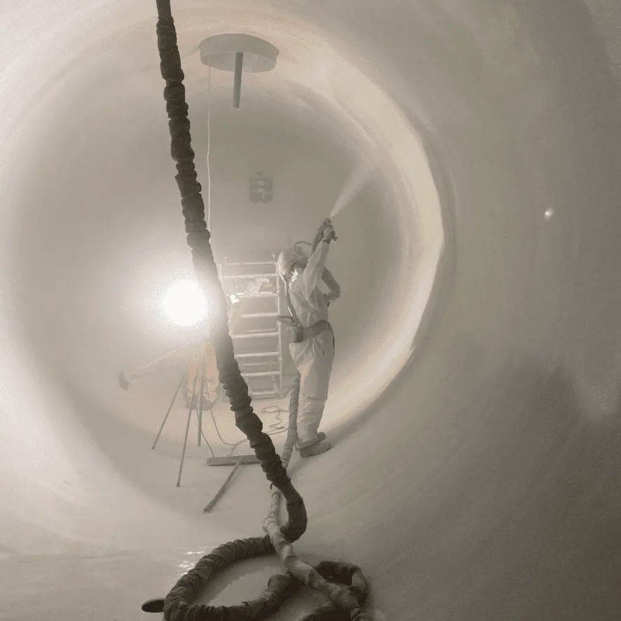 Applicator spraying a protective coating inside an industrial tank